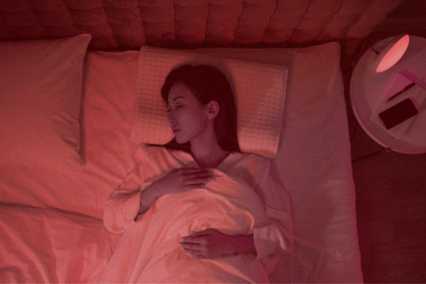 Woman sleeping under red LED light, illustrating nighttime use of red light therapy to support melatonin production and circadian rhythm alignment.